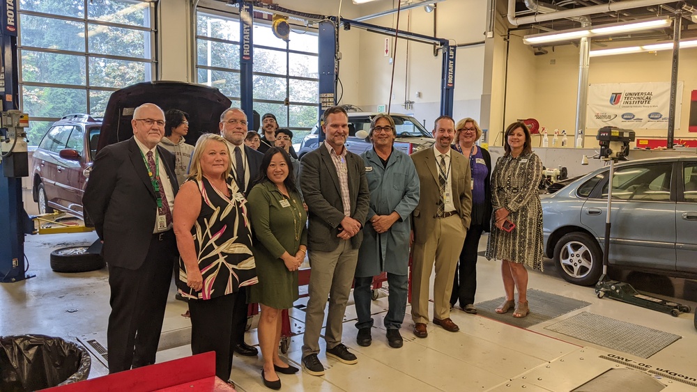 Superintendents, Directors, Students standing in Auto lab with cars and Dynometer